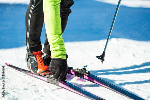 Male professional skier standing on the snow, attaching cross country skis to ski boots, close-up shot.