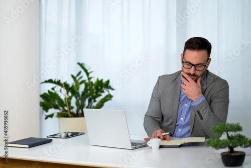 serious young businessman with short stylish beard and glasses sitting at office and taking notes