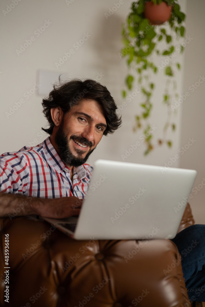 Young business man working at home with laptop on a brown arm chair. Home office concept. Young business man working at home with laptop on a brown arm chair. Home office concept.