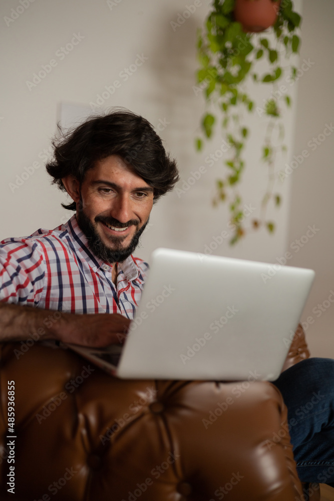 Young business man working at home with laptop on a brown arm chair. Home office concept. Young business man working at home with laptop on a brown arm chair. Home office concept.