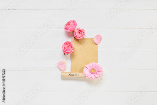 Composition with blank card, word MARCH and flowers on light wooden background. International Women's Day celebration