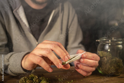Photography Man rolling marijuana cannabis joint in coffee shop Amsterdam with CBD weed buds in glass jars