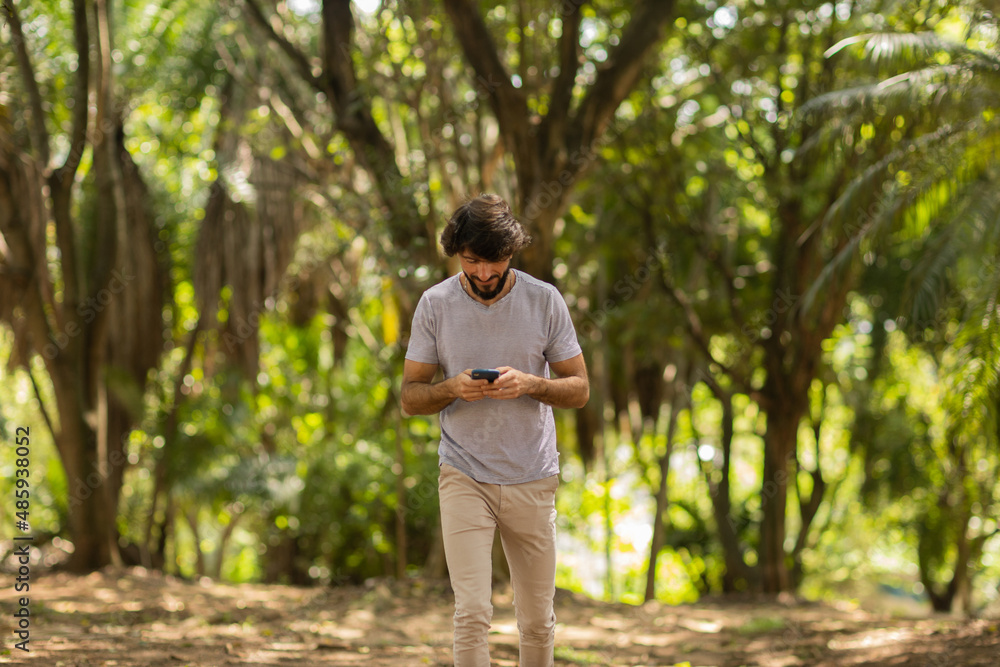 View of young man using a smartphone at day time with a green park in the background. High quality photo View of young man using a smartphone at day time with a green park in the background. High quality photo
