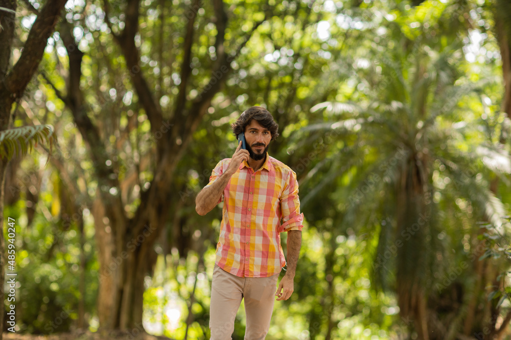 View of young man using a smartphone at day time with a green park in the background. High quality photo View of young man using a smartphone at day time with a green park in the background. High quality photo