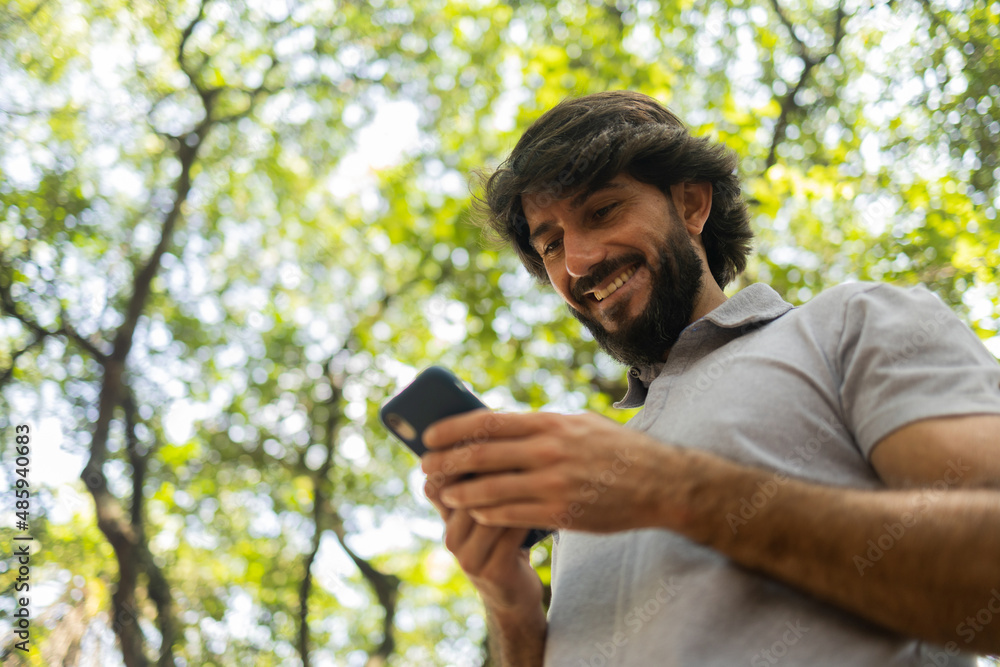 View of young man using a smartphone at day time with a green park in the background. High quality photo View of young man using a smartphone at day time with a green park in the background. High quality photo