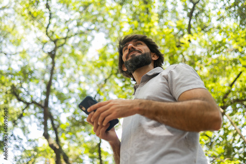View of young man using a smartphone at day time with a green park in the background. High quality photo © Buonaventura