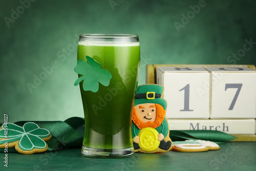 Glass of beer, gingerbread cookies and calendar with date of St. Patrick's Day on green background