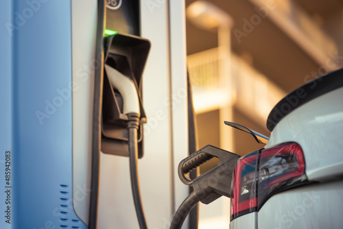 White electric car charging the battery at the charging station on the street, alternative energy concept photo