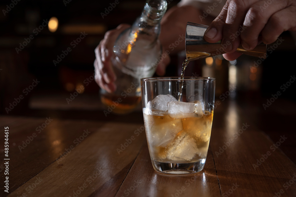 man hand pouring whiskey from jigger into glass man hand pouring whiskey from jigger into glass