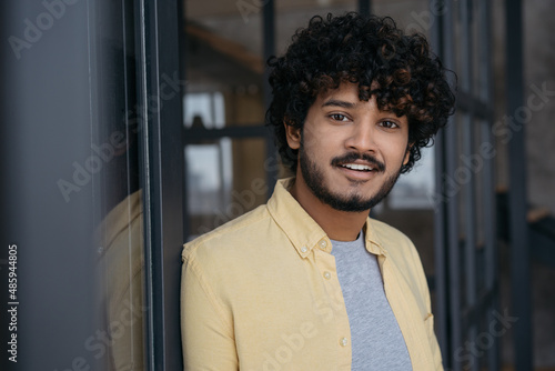 Young smiling Indian man looking at camera standing in modern office. Portrait of handsome successful asian student. Education concept 