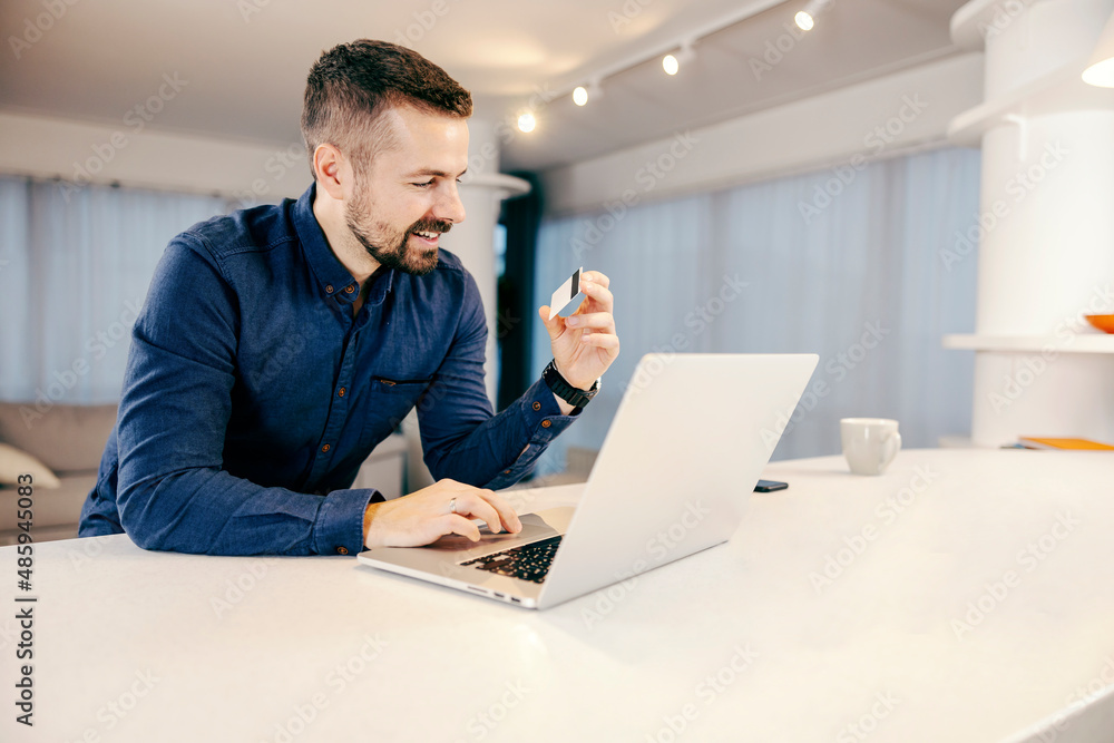 A man using his credit card for online shopping on the laptop from his cozy home. A man using his credit card for online shopping on the laptop from his cozy home.