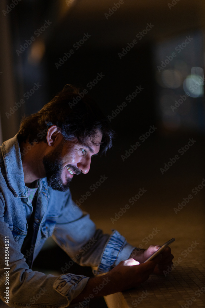 Side view of young man using a smartphone at night time with city view landscape in the background. High quality photo Side view of young man using a smartphone at night time with city view landscape in the background. High quality photo