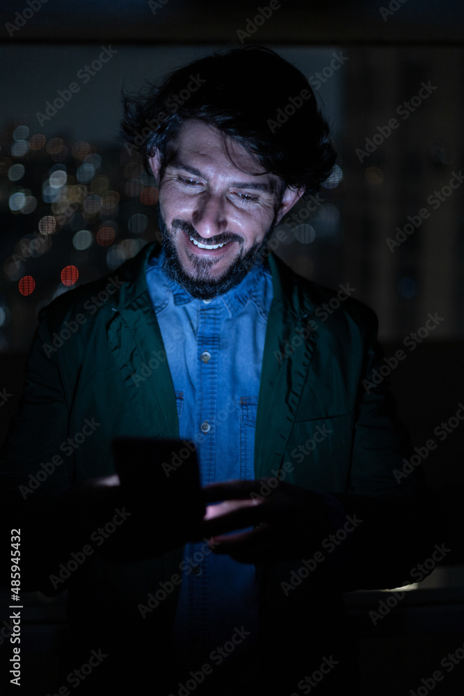 Front view of young man using a smartphone at night time with city view landscape in the background. High quality photo Front view of young man using a smartphone at night time with city view landscape in the background. High quality photo