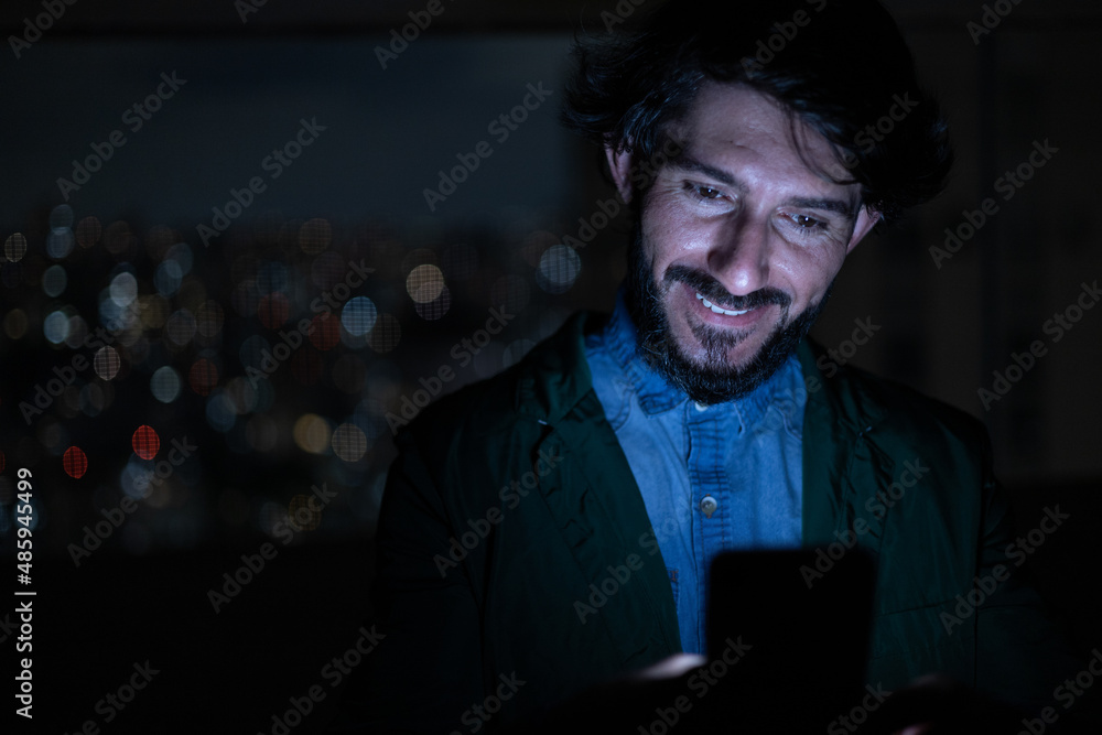 Front view of young man using a smartphone at night time with city view landscape in the background. High quality photo Front view of young man using a smartphone at night time with city view landscape in the background. High quality photo