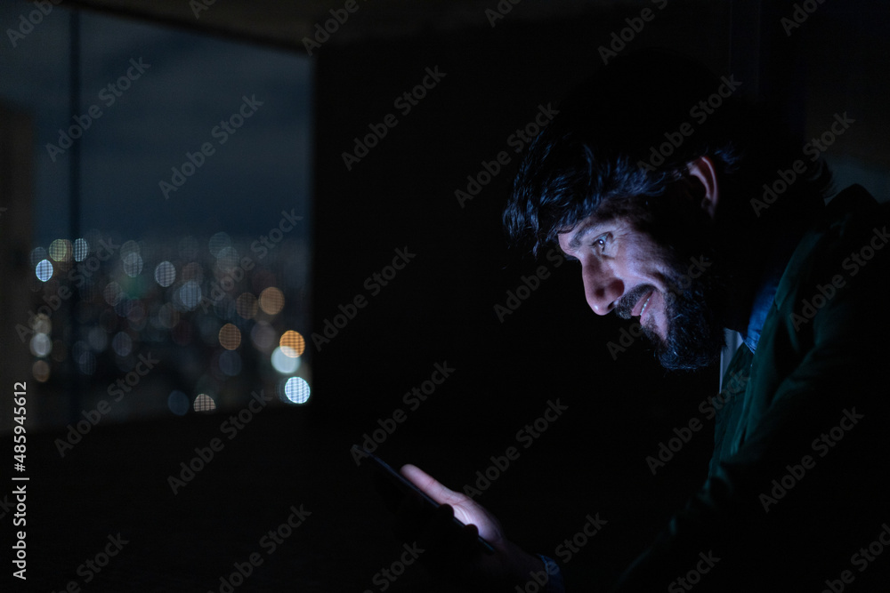 Side view of young man using a smartphone at night time with city view landscape in the background. High quality photo
