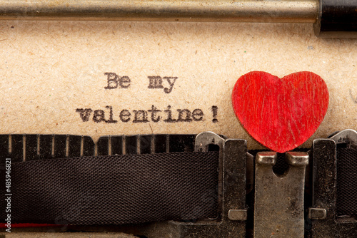 Be my Valentine - phrase on typewriter. Valentines Day greetings concept. Little red wooden heart close up. Valentines greeting card.