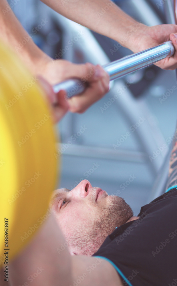 Fototapeta premium Young man lifting the barbell in gym with instructor
