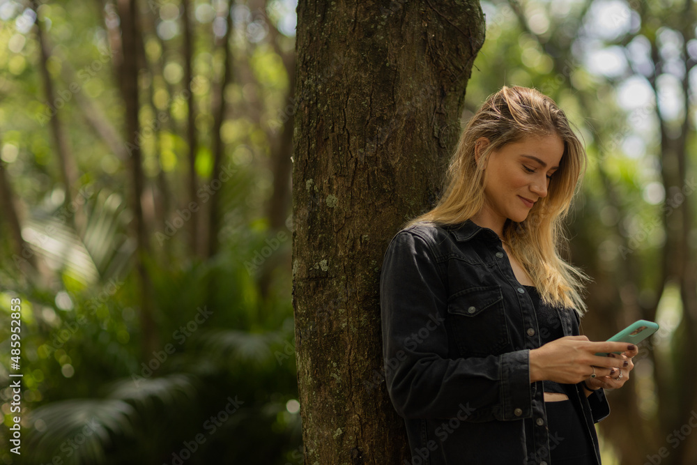 Young woman using a smartphone at day time with a green park in the background. High quality photo Young woman using a smartphone at day time with a green park in the background. High quality photo
