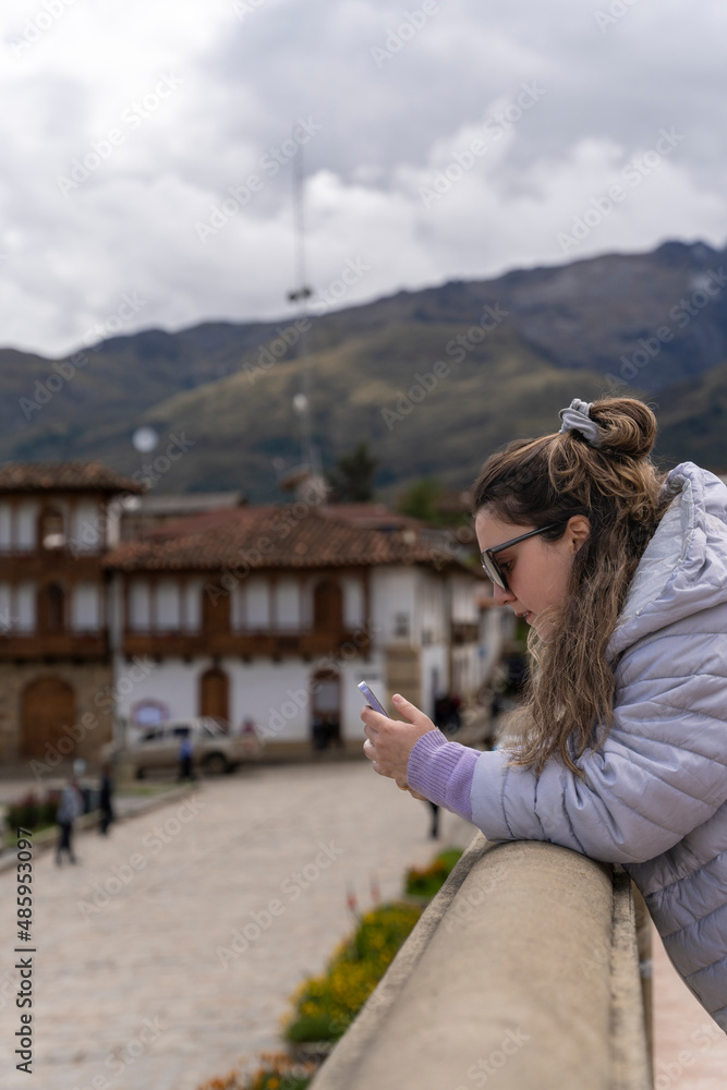 Girl using the mobile while leaning on a traditional andean bridge