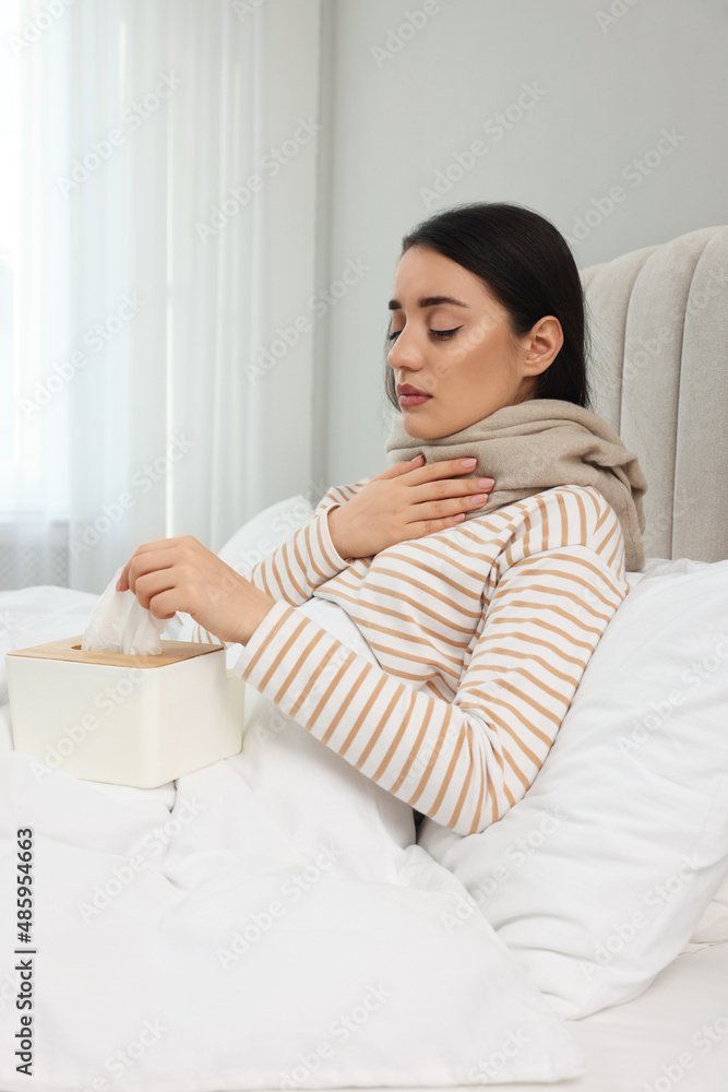 Sick young woman with box of tissues in bed at home