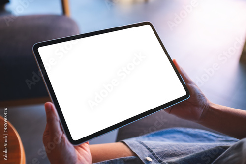 Mockup image of a woman holding digital tablet with blank white desktop screen in cafe