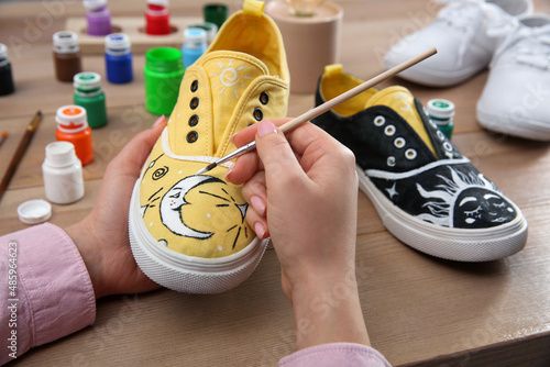 Woman painting on sneaker at wooden table, closeup. Customized shoes photo