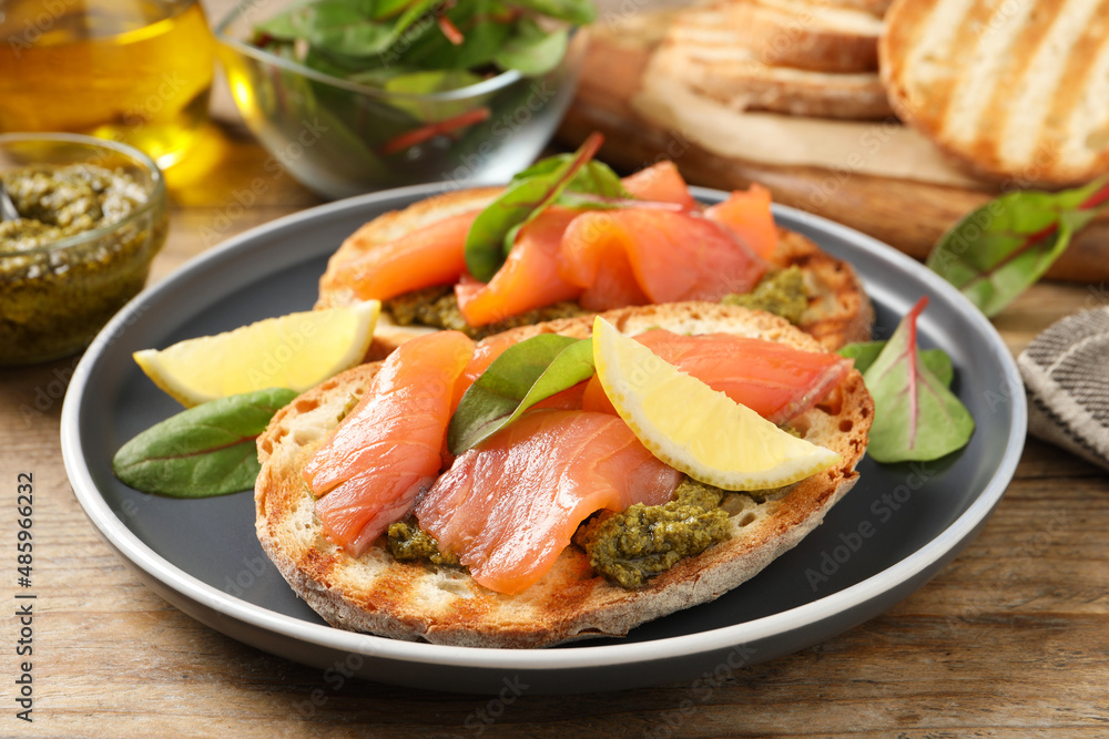 Delicious bruschettas with salmon and pesto sauce on wooden table, closeup