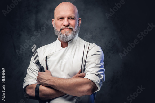 Bald elderly chef with kitchen spatula and tongs photo