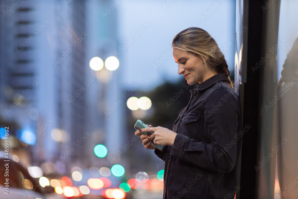 Young woman using a smartphone at night time with city view landscape in the background. High quality photo Young woman using a smartphone at night time with city view landscape in the background. High quality photo