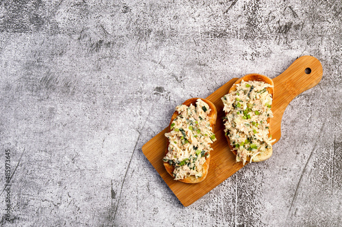 Tuna Salad open faced Sandwiches on a small cutting wooden board on a dark grey background. Top view, flat lay