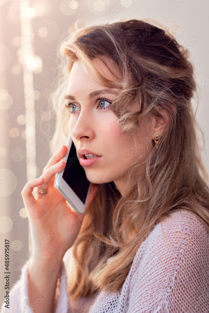 beautiful young brunette with long hair talking on a smartphone, looking out the window, portrait of an attractive woman using the phone beautiful young brunette with long hair talking on a smartphone, looking out the window, portrait of an attractive woman using the phone