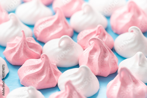 white and pink swiss meringues kiss cookies over blue background, close up © Alisa