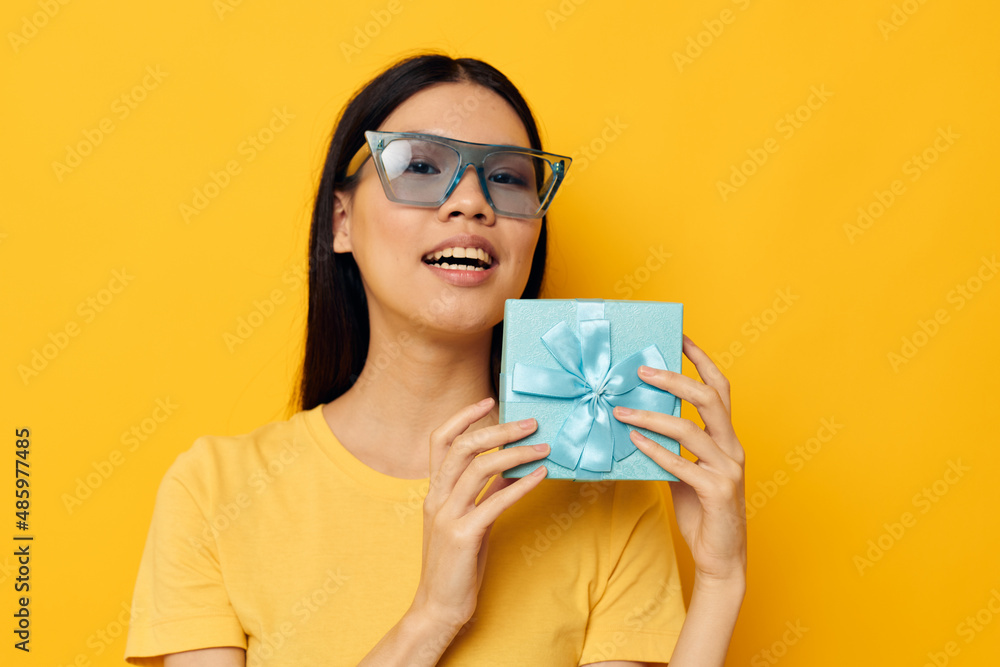 Portrait Asian beautiful young woman with a gift in glasses holiday yellow background unaltered Portrait Asian beautiful young woman with a gift in glasses holiday yellow background unaltered
