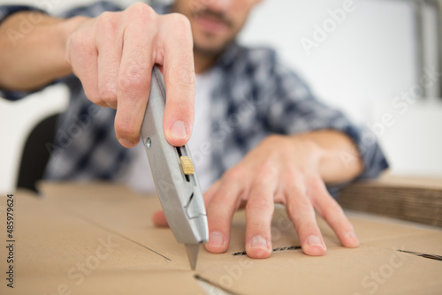 man using an utility knife to open a cardboard box