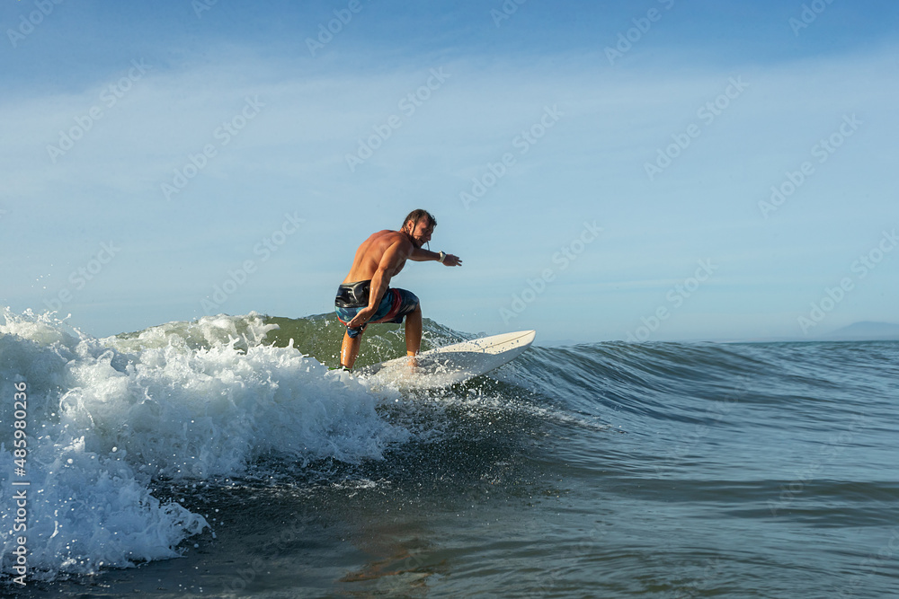 Young surfer with lean muscular body rides the tropical wave