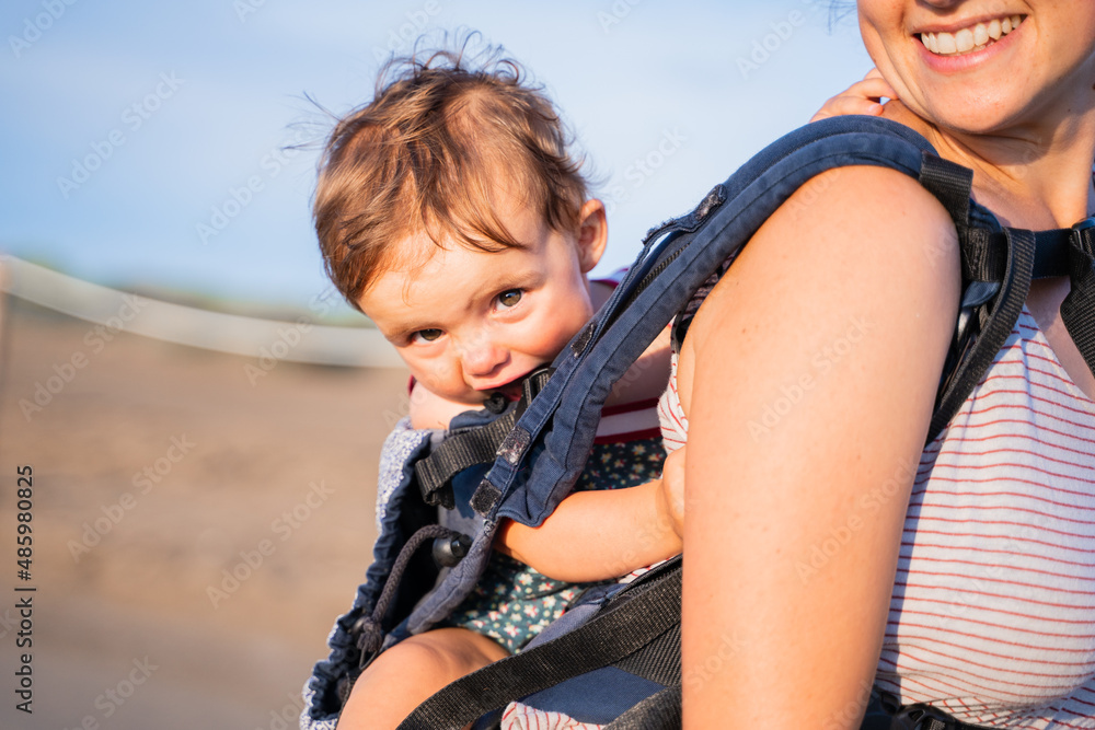 Baby chewing on the strap of a baby carrier outdoors