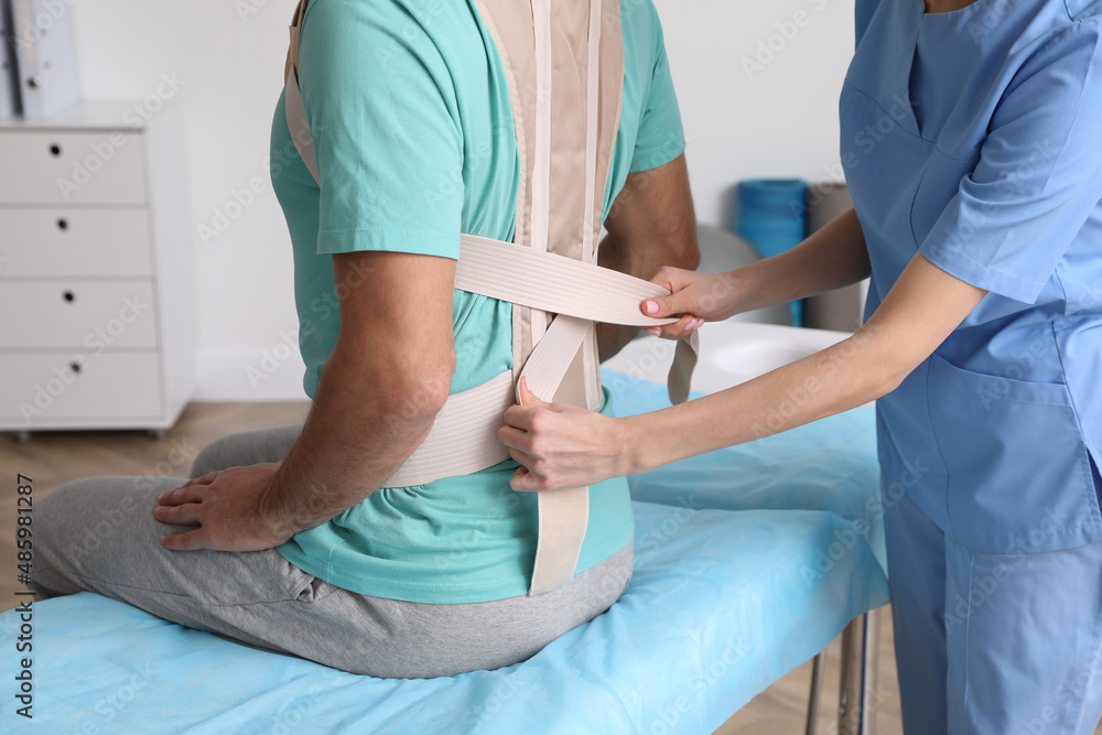 Orthopedist helping patient to put on posture corrector in clinic, closeup. Scoliosis treatment Orthopedist helping patient to put on posture corrector in clinic, closeup. Scoliosis treatment