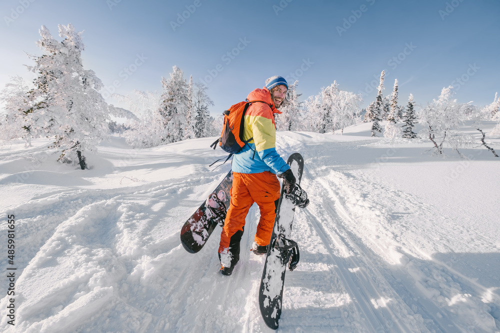 Snowboarder walking with a snowboard in the winter forest. Ski touring in the snowy mountains on a sunny day