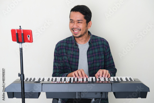 Adult Asian man smiling happy when learning playing piano on online course photo