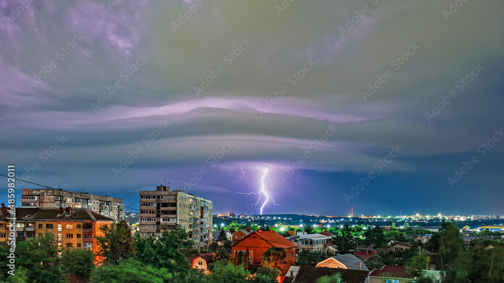 Thunderstorm over the city at night, bright lightning among dense clouds