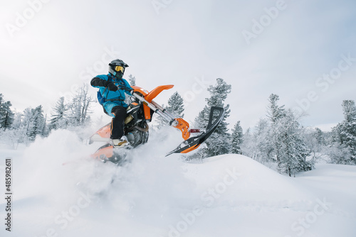 Snowbike rider in mountain valley in beautiful snow powder. Modify dirt bike with snow splashes and trail. Snowmobile sport riding, winter sunny day © Annatamila