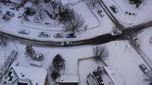 An aerial view of a suburban neighborhood after a nor'easter storm. It is a cloudy day with everything covered in snow. The camera tilted down truck left over the houses and snow covered street. photo