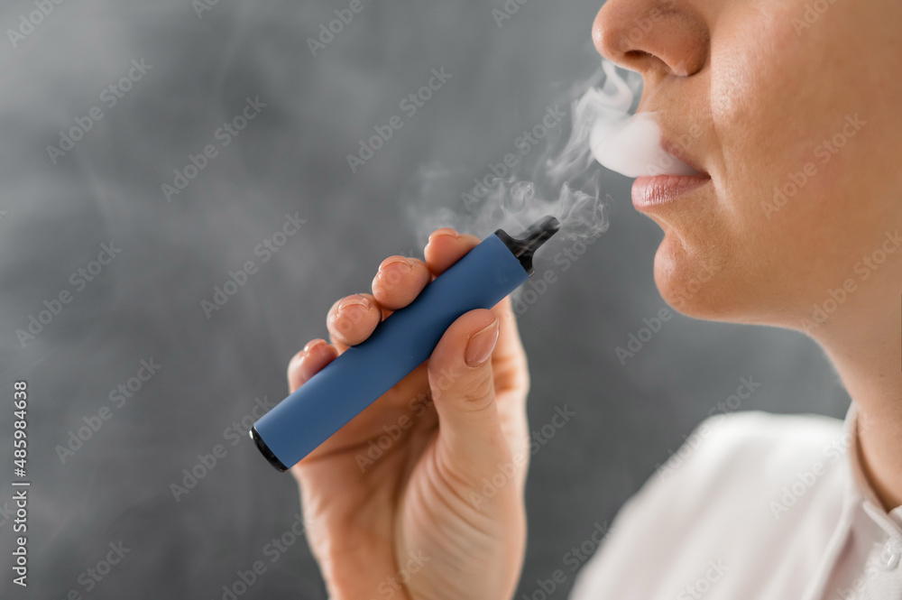 Obraz premium Caucasian woman smokes a disposable vape in the studio.