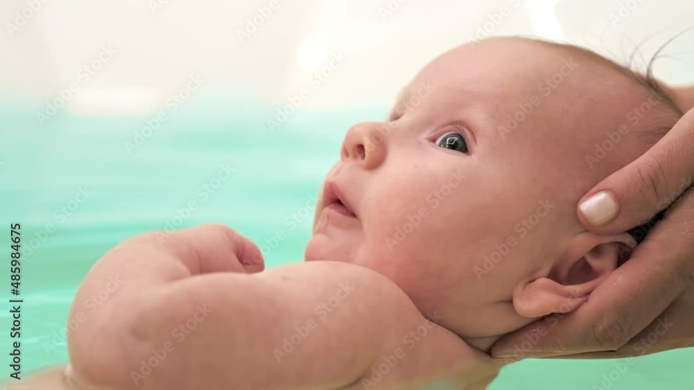 SLOW MOTION: Mom teaches a newborn baby to swim and stay on the water. Two-month-old baby is bathing in a large bathtub. Newborn baby is in the water, bathroom. Hygiene procedures of a newborn boy SLOW MOTION: Mom teaches a newborn baby to swim and stay on the water. Two-month-old baby is bathing in a large bathtub. Newborn baby is in the water, bathroom. Hygiene procedures of a newborn boy