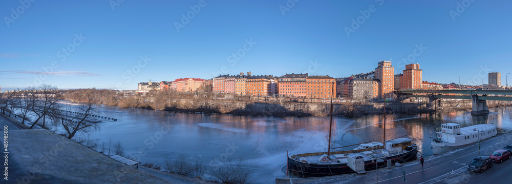 View over the canal Karlbergskanalen with ice floes and an old boat, apartment houses and the bridge St Eriksbron with tower houses a winter day in Stockholm