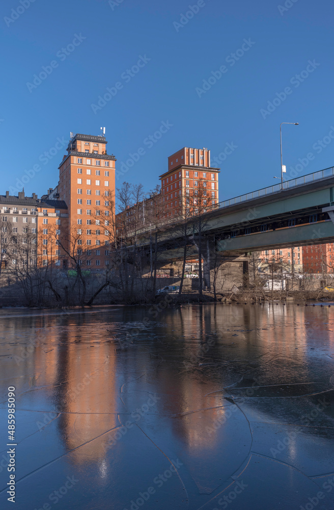 The bridge St Eriksbron over the canal Karlbergskanalen with ice floes, apartment houses and offices and the traffic route Karlbergsleden a sunny winter day in Stockholm