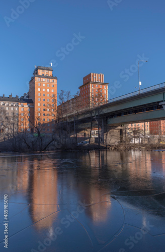 The bridge St Eriksbron over the canal Karlbergskanalen with ice floes, apartment houses and offices and the traffic route Karlbergsleden a sunny winter day in Stockholm