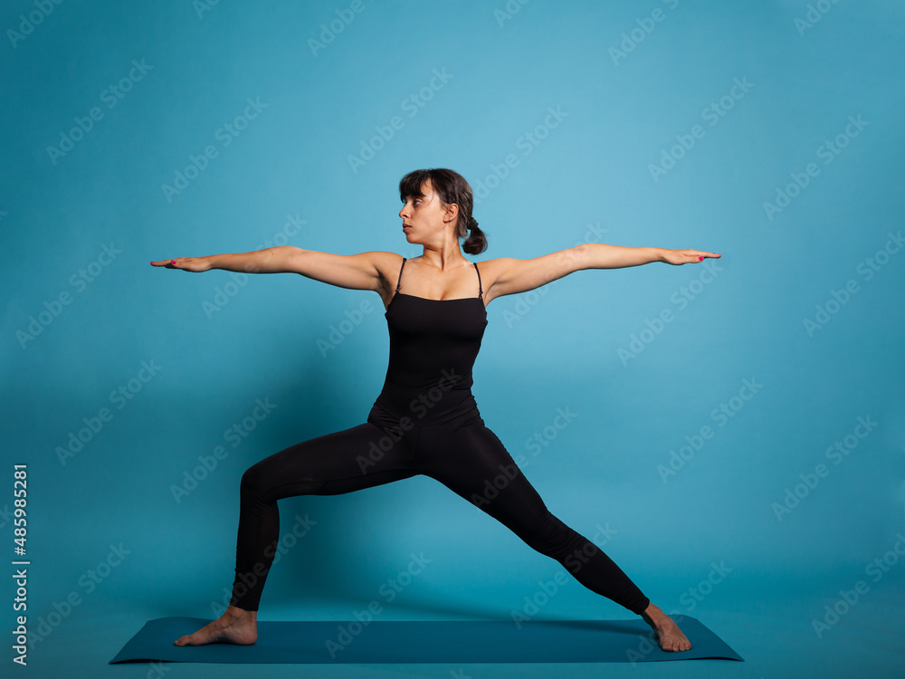 Obraz premium Personal trainer standing up on yoga mat practicing sport exercices stretching body muscles. Athlete woman in sportswear trying fitness posture working at healthy lifestyle. Active person concept