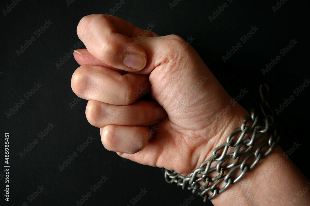 hands clenched into fists in handcuffs in the form of chains on a black