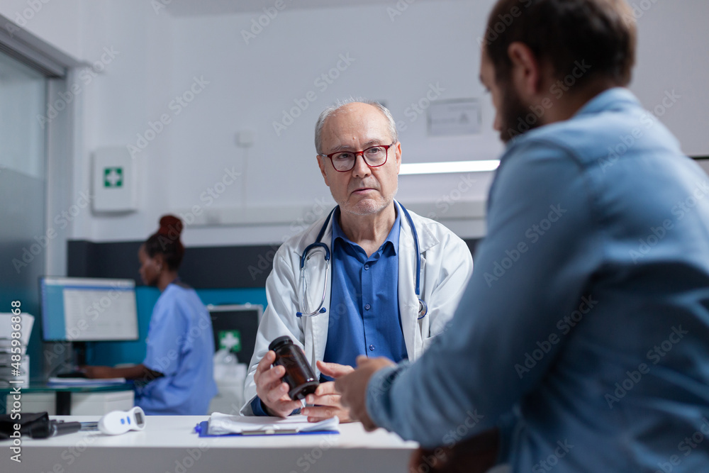 Medic showing bottle of pills to patient at examination appointment, giving jar with prescription medicine to cure illness. General practitioner holding healthcare treatment for young man. Medic showing bottle of pills to patient at examination appointment, giving jar with prescription medicine to cure illness. General practitioner holding healthcare treatment for young man.